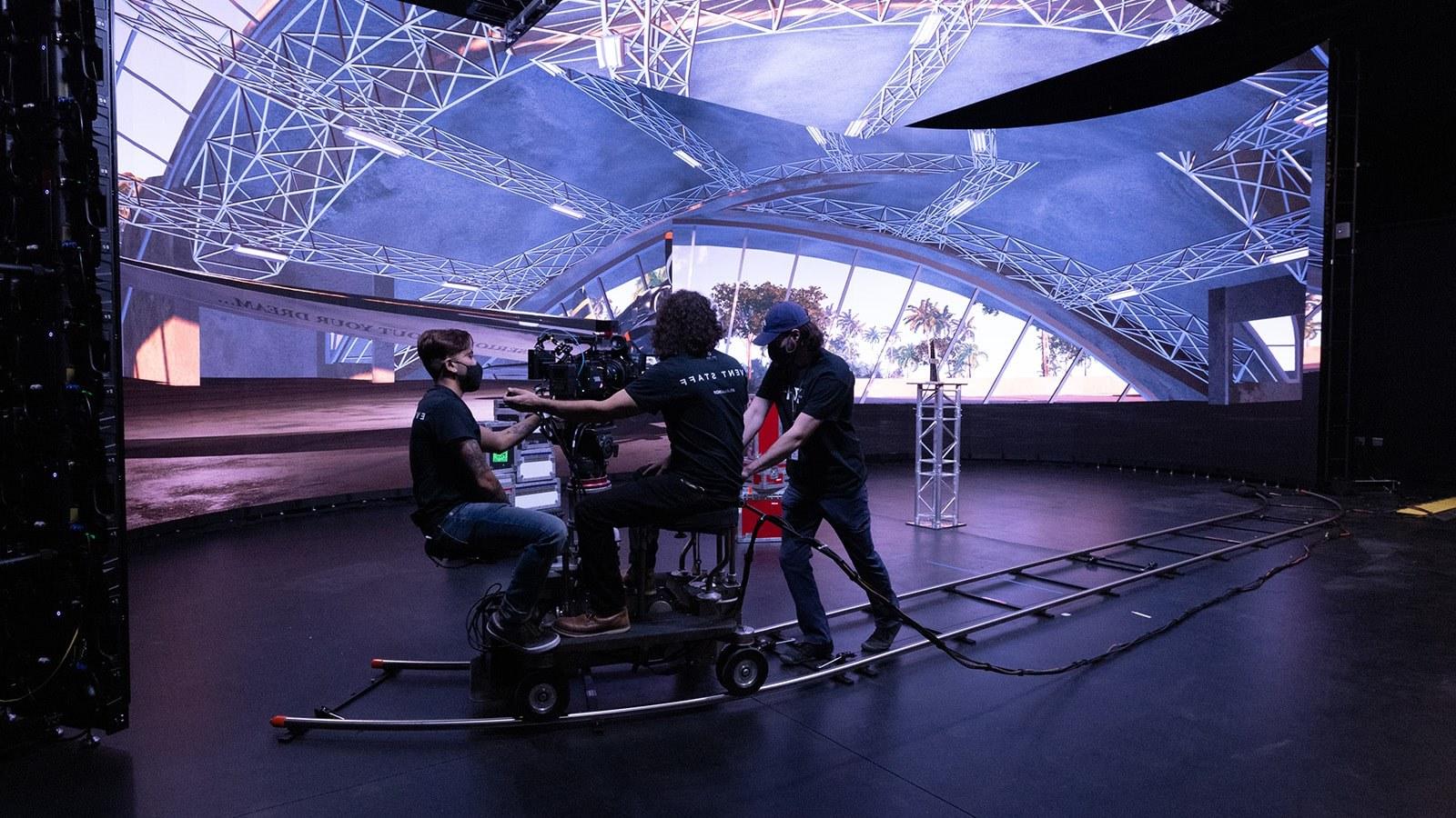 Crew members work on a dolly-mounted camera. A virtual production LED screen displays the interior of an airplane hangar